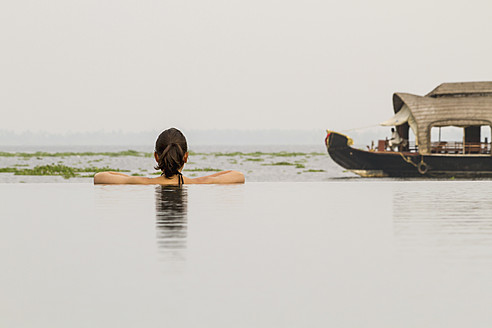 Indien, Kerala, Junge Frau im Schwimmbad schaut auf Hausboot - MBEF000499