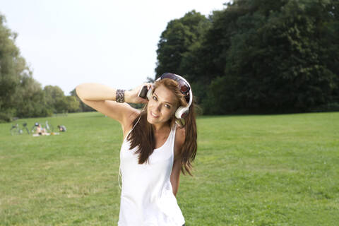 Deutschland, Berlin, Junge Frau hört Musik im Treptower Park, lizenzfreies Stockfoto