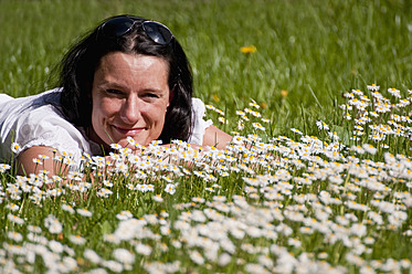 Germany, Bavaria, Mid adult woman relaxing in meadow, daisy flowers in foreground - UMF000457