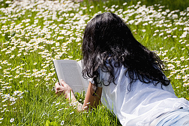 Deutschland, Bayern, Mittlere erwachsene Frau liest Buch auf Wiese, Gänseblümchen im Hintergrund - UMF000458