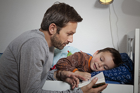 Deutschland, Berlin, Vater liest Buch, während Sohn schläft - RBF000946