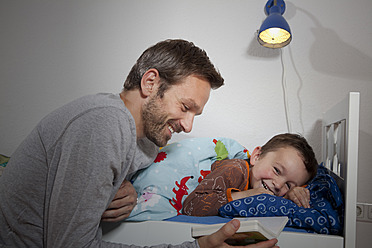 Germany, Berlin, Father reading book while son sleeping - RBF000947