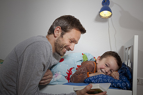 Deutschland, Berlin, Vater liest Buch, während Sohn schläft - RBF000947