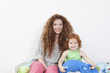 Germany, Berlin, Mother and daughter sitting on bed, smiling, portrait - RBF000990