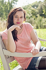 Germany, Berlin, Young woman sitting on park bench, smiling, portrait - BFRF000057