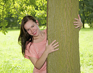 Germany, Berlin, Young woman embracing tree trunk, smiling, portrait - BFRF000060