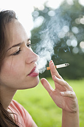 Germany, Berlin, Young woman smoking cigarette in park - BFRF000061