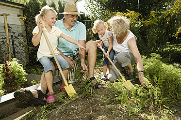 Deutschland, Bayern, Großeltern mit Kindern arbeiten im Gemüsegarten - RNF001017