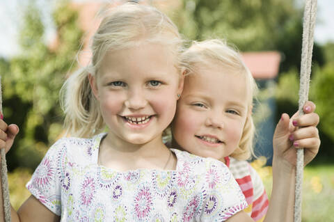 Germany, Bavaria, Girls swinging on swing, smiling, portrait stock photo