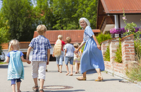 Deutschland, Bayern, Ältere Frau mit Kindern tanzt auf der Straße, lizenzfreies Stockfoto