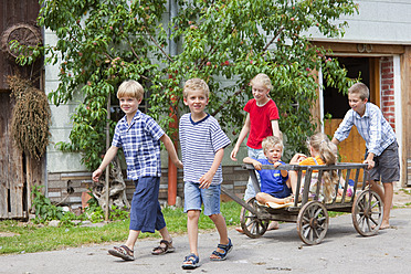 Deutschland, Bayern, Gruppe von Kindern, die mit einem Handwagen vor einem Bauernhaus spielen - HSIYF000133