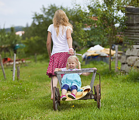 Germany, Bavaria, Mother pulling daughter in hand cart through meadow - HSIYF000142