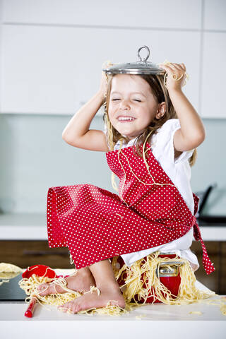 Deutschland, Mädchen spielt mit Spaghetti auf Küchenarbeitsplatte, lizenzfreies Stockfoto