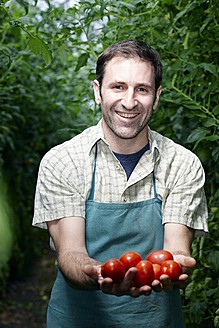 Deutschland, Bayern, München, Älterer Mann hält Tomaten im Gewächshaus - RREF000046