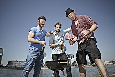 Germany, Cologne, Young men gathered around barbecue and drinking beer - RHYF000216