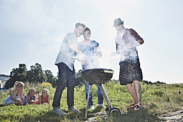 Deutschland, Köln, Männer grillen Würstchen und Frauen im Hintergrund - RHYF000222