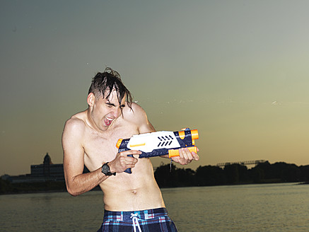 Deutschland, Düsseldorf, Junger Mann mit Wasserpistole am Flussufer - STKF000032