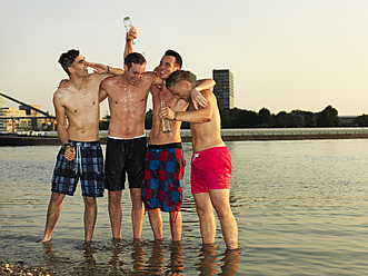 Germany, Duesseldorf, Young friends drinking beer at riverbank - STKF000043