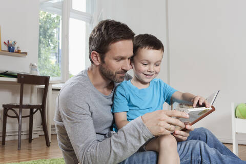Deutschland, Berlin, Vater und Sohn lesen ein Buch, lizenzfreies Stockfoto