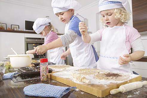 Deutschland, Mädchen und Junge backen Tassenkuchen und streuen Zuckerstreusel - FKF000090