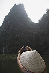 Vietnam, Ninh Binh, Junger Tourist beim Fotografieren der Landschaft - MBEF000524