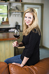 USA, Texas, Blonde Frau sitzt auf dem Sofa und hält ein Glas Rotwein in der Hand - ABAF000287