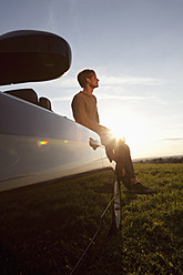 Germany, Bavaria, Mid adult man sitting on car - RBF001097