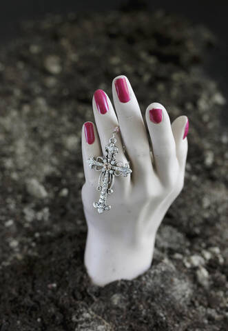 Human hand of mannequin with crucifix in soil at cemetery stock photo