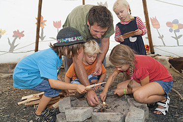 Germany, Munich, Father with children preparing camp fire in tent - TCF002996