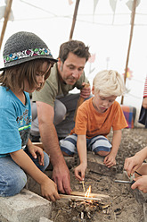 Germany, Munich, Father with children preparing camp fire in tent - TCF002997