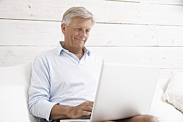 Spanien, älterer Mann, der lächelnd seine E-Mails auf dem Laptop überprüft - PDYF000120