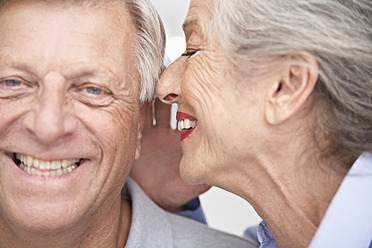 Spain, Senior woman whispering into ear of man, smiling - PDYF000157