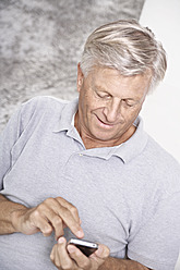 Spain, Senior man checking emails on mobile, smiling - PDYF000169