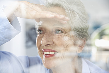 Spanien, ältere Frau schaut durch das Fenster, lächelnd - PDYF000180