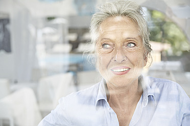 Spain, Senior woman looking through window, smiling - PDYF000181