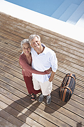 Spanien, älteres Paar mit Koffer am Schwimmbad, lächelnd, Porträt - PDYF000194