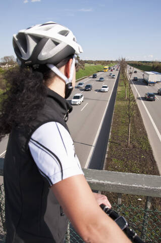 Deutschland, Mittlere erwachsene Frau mit Mountainbike auf Brücke mit Blick auf den Verkehr auf der Autobahn, lizenzfreies Stockfoto