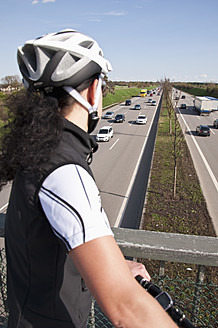 Deutschland, Mittlere erwachsene Frau mit Mountainbike auf Brücke mit Blick auf den Verkehr auf der Autobahn - UMF000512