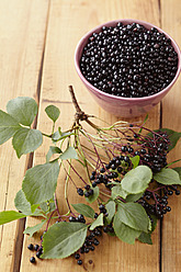 Bowl full of elderberries with branch on wooden table - ECF000120