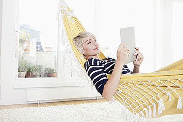 Germany, Bavaria, Munich, Woman relaxing in hammock and watching digital tablet - RBYF000222