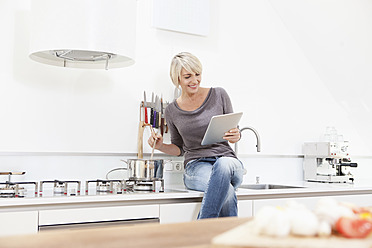 Germany, Bavaria, Munich, Woman watching digital tablet and preparing food - RBYF000230