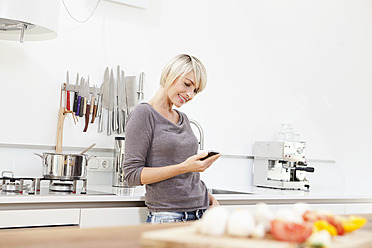 Deutschland, Bayern, München, Frau benutzt Handy in Küche - RBYF000232