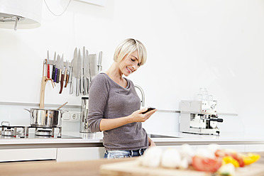 Germany, Bavaria, Munich, Woman using mobile in kitchen - RBYF000232