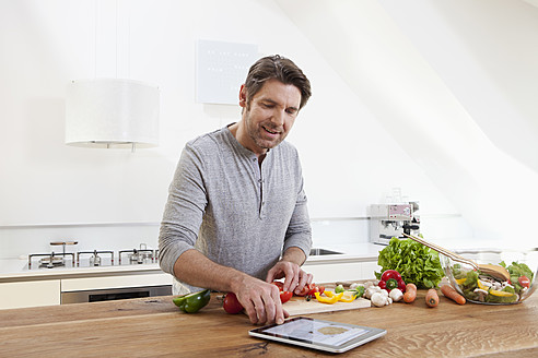 Deutschland, Bayern, München, Mann bereitet Essen vor und schaut auf ein digitales Tablet - RBYF000254