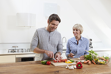Germany, Bavaria, Munich, Mature couple chopping vegetables in kitchen, smiling - RBYF000257