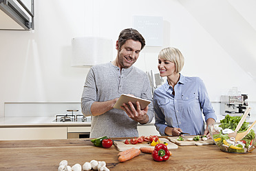 Deutschland, Bayern, München, Älteres Paar bei der Essenszubereitung mit Blick auf digitales Tablet - RBYF000258