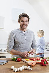 Germany, Bavaria, Munich, Mature man chopping vegetables, woman standing in background - RBYF000260