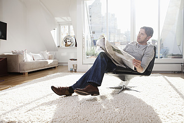 Germany, Bavaria, Munich, Man reading newspaper in living room - RBYF000285