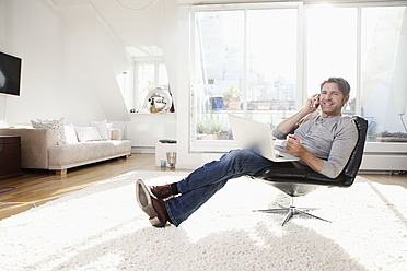 Germany, Bavaria, Munich, Man using laptop in living room - RBYF000289