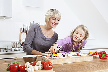 Germany, Bavaria, Munich, Mother and daughter preparing pizza in kitchen - RBYF000296